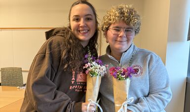 Two women stand together smiling and holding flowers