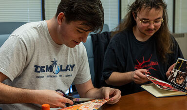Two students make scrapbooks while sitting at a table.