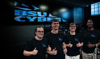 Four students give thumbs up while standing in front of a screen with the BSU Cyber logo.