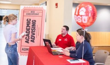 Darren Smith sits at a table and talks to a fellow student who is standing in front of table