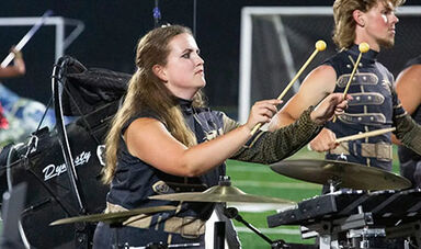 Delaney Hughes plays percussion instruments on a football field.