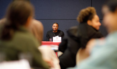 A man sits at the front of the room with students listening to him talk