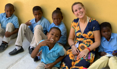 Ellie Roberts smiles sitting on the ground with some of her students