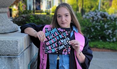 A woman stands holding her graduation cap