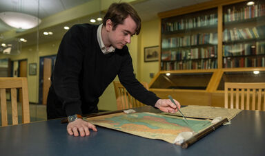 A man stands over a desk looking at a map