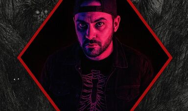 A man wears a baseball cap backwards staring at camera with menacing look