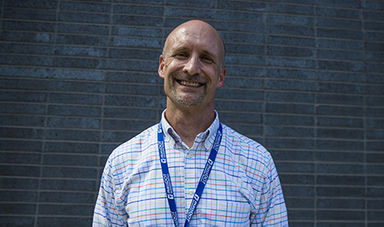 Loren Herren smiling and standing in front of a gray wall.