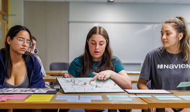 Three students look at a display featuring a map.
