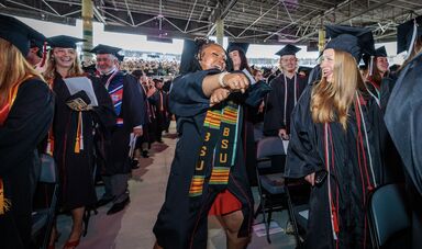 A graduate dances in the aisle as others cheer her on enthusiastically.