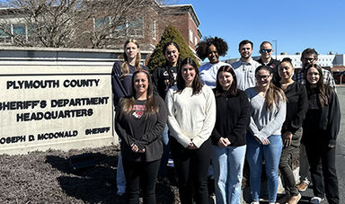 Outside students stand in a group next to a Plymouth County Sheriff's Department sign.