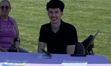A young man sits at a table and smiles
