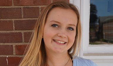 Riley Lathrop standing in front of a brick wall and window