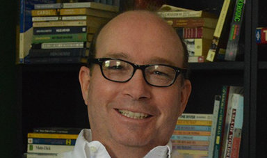 Arthur Lizie smiles in front of a bookshelf.