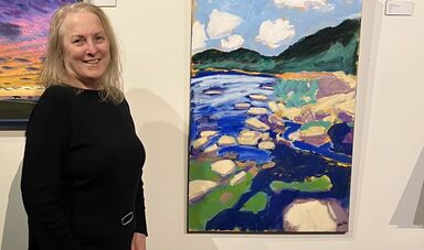 A woman stands smiling next to a piece of artwork