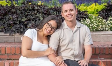 Maddie Monagle and Jonny Matthews sit close together on an outdoor bench,