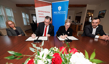 BSU and IHP leaders sign an agreement while sitting at a large tables with flowers in front of them.