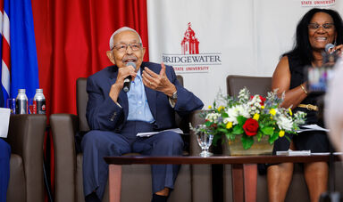A man sits holding a microphone smiling and talking