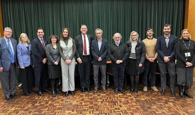 A group of people stand, smiling in front of a curtain