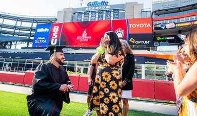 A graduate proposes on the Gillette Stadium field before commencement.
