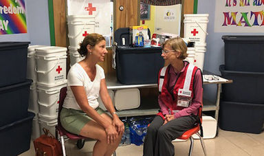 Maggie Lowe, wearing a Red Cross vest, talks with a flood victim.