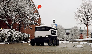 A food delivery robot travels on a campus sidewalk.