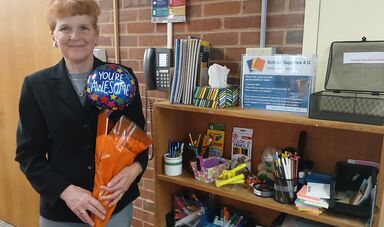 A woman stands holding flowers next to a bookshelf