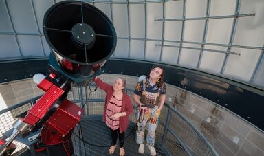 Two people look up while using a telescope inside a large dome.