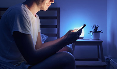 A person texts on a phone while sitting on a bed.