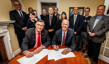 UMass and BSU administrators stand around a table to sign a document.