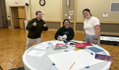 A group of people are at a table painting and smiling