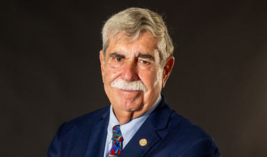 Headshot of Mike Vieira in front of a black background wearing a suit and tie.