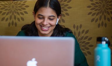 Woman is smiling while looking down at her laptop
