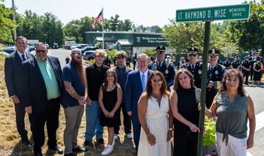 A group of people stands next to a sign for Raymond Wise Drive