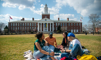 Four students sitting on blankets in front of Boyden Hall on an early spring day