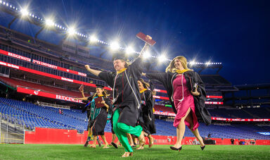 Graduates running across the field at Gillette Stadium in their commencement regalia