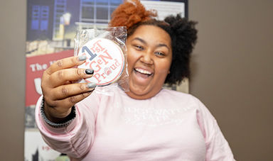 A student smiles and poses with a cookie that says &quot;First Gen Proud&quot;