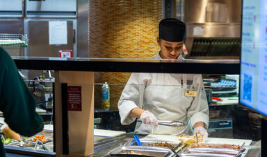 A dining services employee preparing food in the Bear's Den