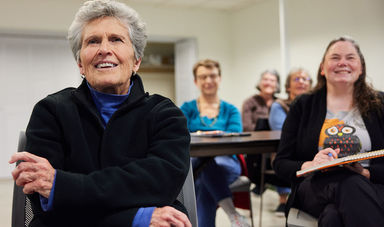A class of senior college students smiling as they listen to their lecture