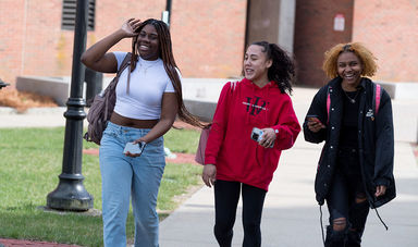 Three students smiling and laughing as they walk outside on campus