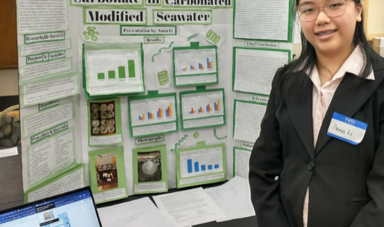 A student standing in front of a science fair presentation board on seawater