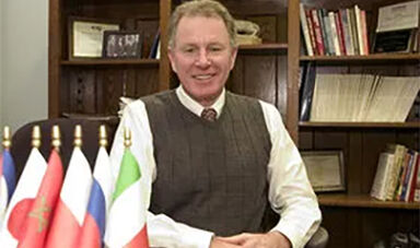 Dr. Edward W. Minnock sits at a desk with a row of small international flags