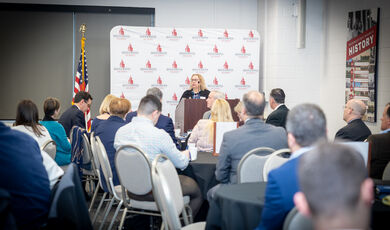 A woman stands at a podium talking to a crowd sitting in front of her 