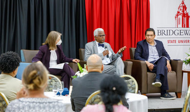 Three people sit on stage talking to people at tables in front of them