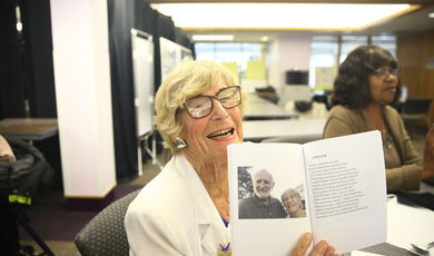 Frances Sharon smiles while holding up a book that contains a photo of her and a man 