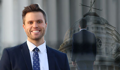 Kyle Bueno stands with a smile in the background is blurred image of him looking up at Boyden Hall 