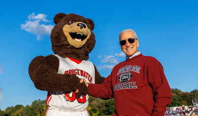 A bear mascot shakes hands with a man in a red sweatshirt