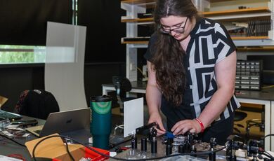 Ava Bickford stands over a table adjusting optical equipment.