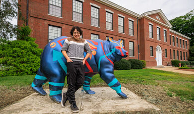 A young man stands in front of a blue painted bear