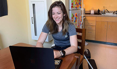 Abigail Adams works on her computer sitting at a kitchen table.