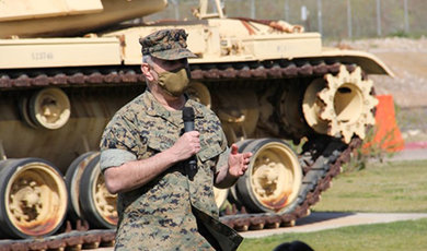 Anthony LaCourse speaks to a crowd standing in front of a tank.